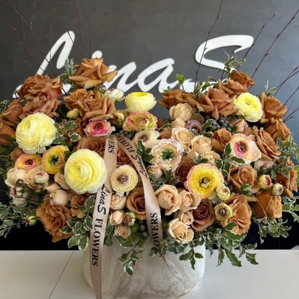 Large mixed floral arrangement in a round box with tan and yellow blooms