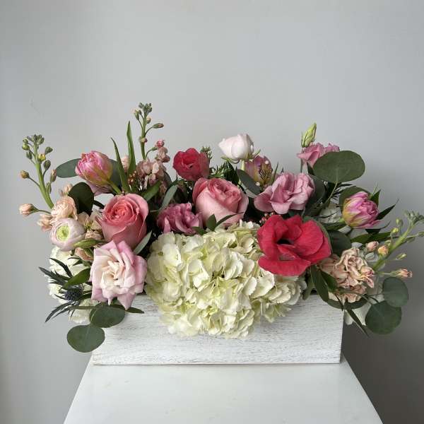 Mixed pink and white flowers arranged in a white wooden box
