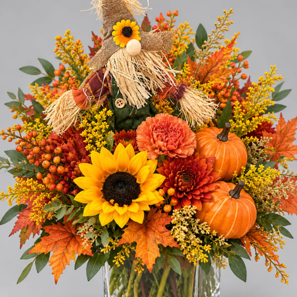 Fall bouquet with sunflowers, mums, pumpkins, and a scarecrow in a glass vase