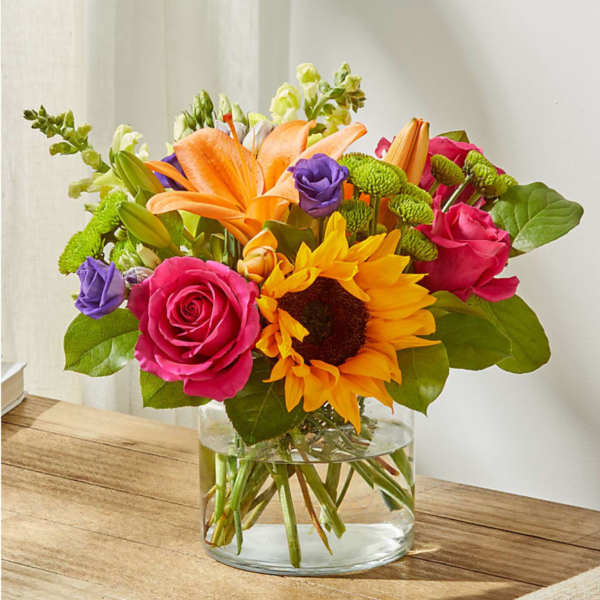 Bright mixed bouquet with sunflowers, roses, lilies, and a glass vase