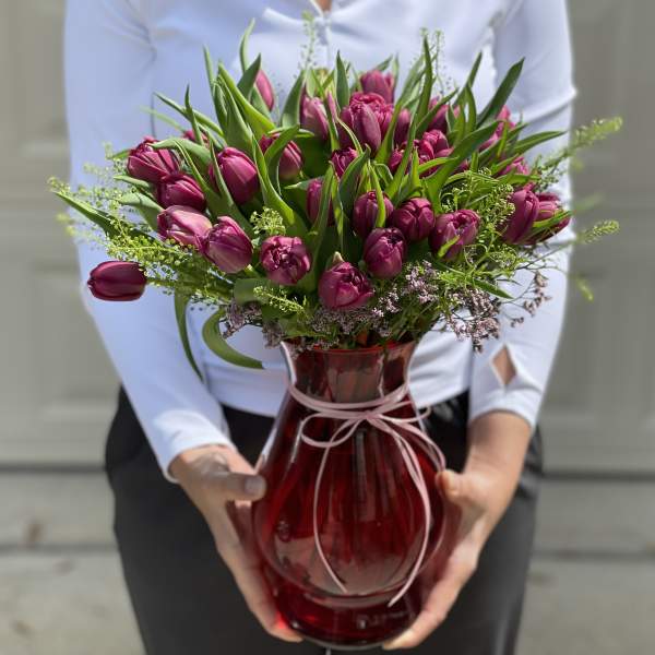Magenta tulip bouquet in a red glass vase with a pink ribbon