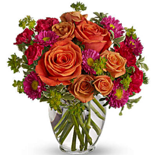 Orange roses and magenta daisies in a clear glass vase