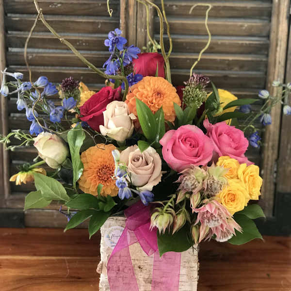 Mixed bouquet of roses, dahlias, and blue flowers in a white box with pink ribbon