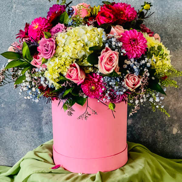 Pink and yellow mixed flower arrangement in a round pink box