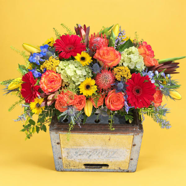 Bright mixed bouquet in a rustic metal container with red, orange, yellow, and blue flowers