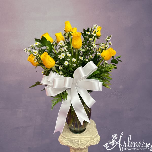 Yellow roses and white daisies in a glass vase with a white ribbon