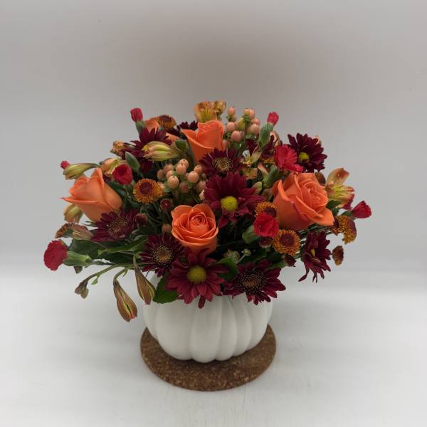 Orange roses and burgundy daisies in a white pumpkin vase