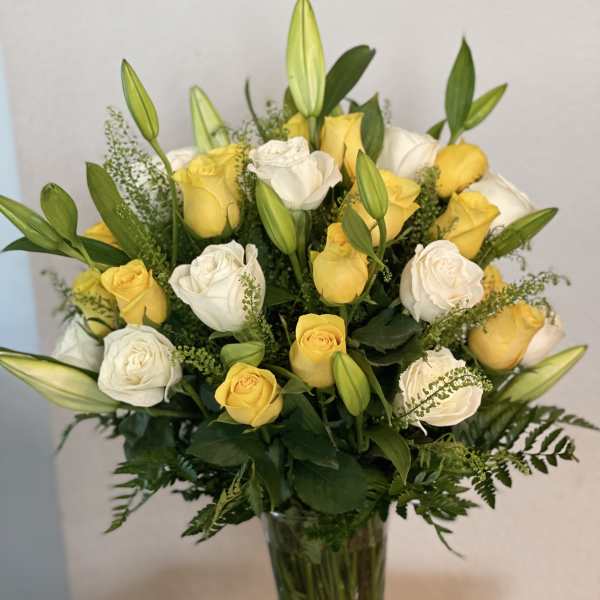 Yellow and white roses arranged in a tall glass vase