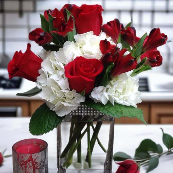 Red roses and white hydrangeas in a glass vase with a candle nearby