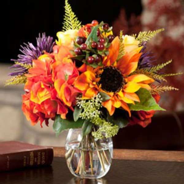 Bright autumn bouquet in a clear glass vase with sunflowers and orange blooms