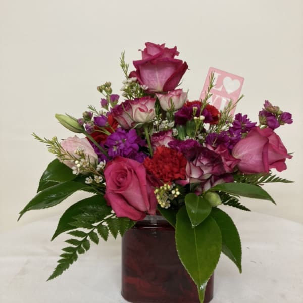 Pink and purple rose bouquet in a square vase with a small love card
