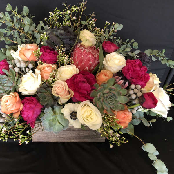 Low floral arrangement with roses, protea, and succulents in a wooden box