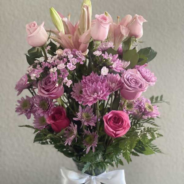 Pink roses and lilies arranged in a glass vase with a white ribbon