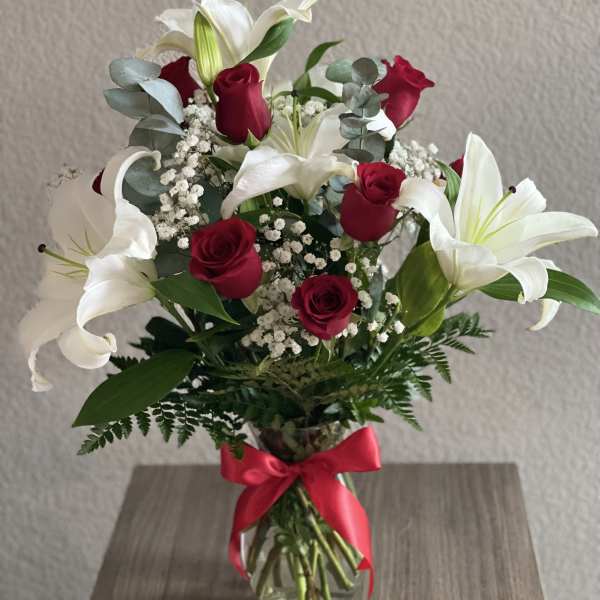 Bouquet of red roses and white lilies in a glass vase with a red ribbon