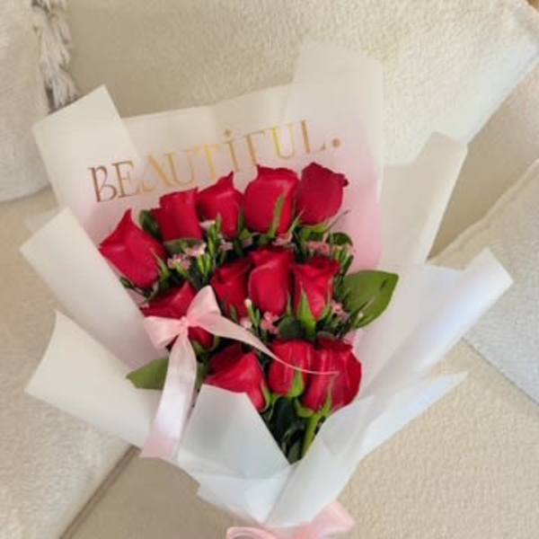Bouquet of red roses wrapped in white paper with a pink ribbon