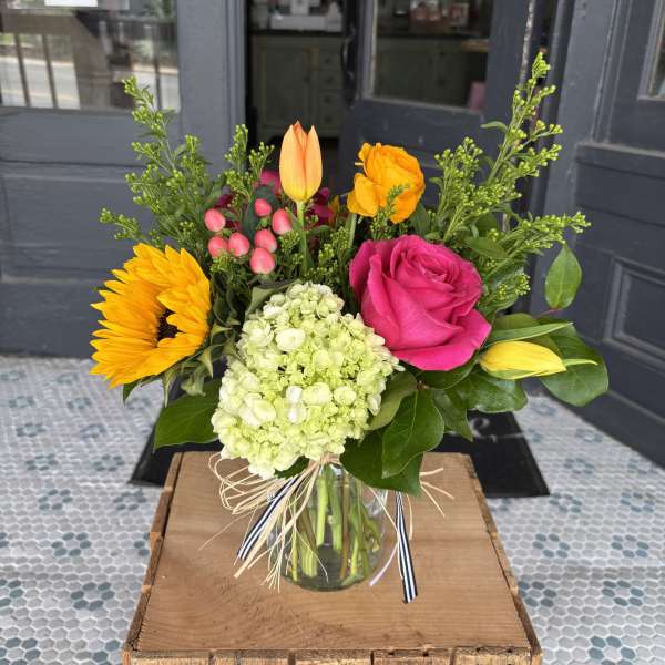 Mixed bouquet in a glass vase with a pink rose, sunflower, hydrangea, and tulips