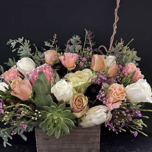 Low arrangement of peach and white roses with protea and succulents in a rustic wooden box