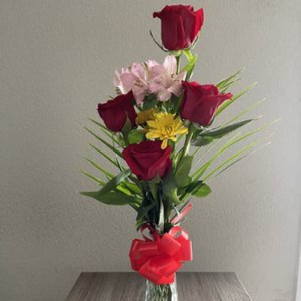 Tall bouquet of red roses and pink flowers in a glass vase with a red bow