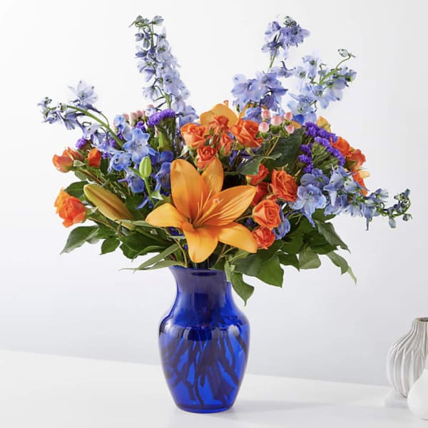 Colorful bouquet with orange lilies and blue flowers in a cobalt vase