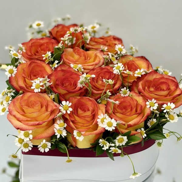 Low arrangement of orange and yellow roses with white daisies in a white hat box container