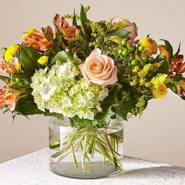 Mixed bouquet with a peach rose, hydrangea, and orange alstroemeria in a glass vase