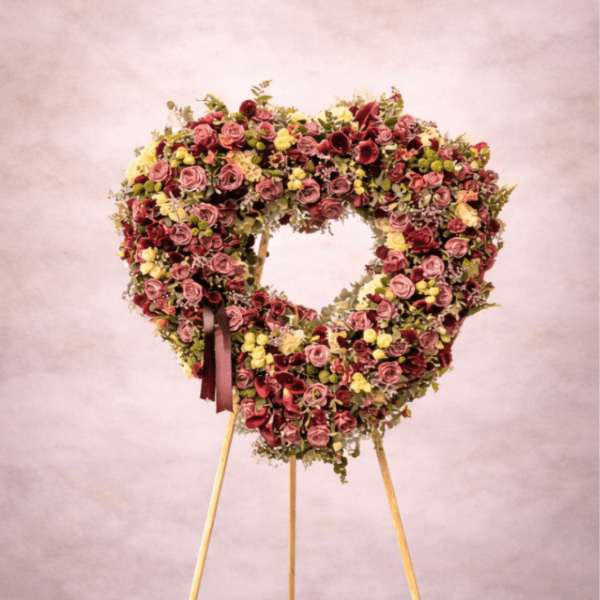Heart-shaped standing wreath of mauve and yellow flowers on a wooden easel stand