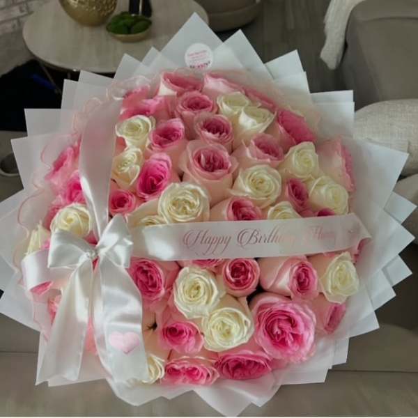 Pink and white rose bouquet wrapped in white paper with a satin bow