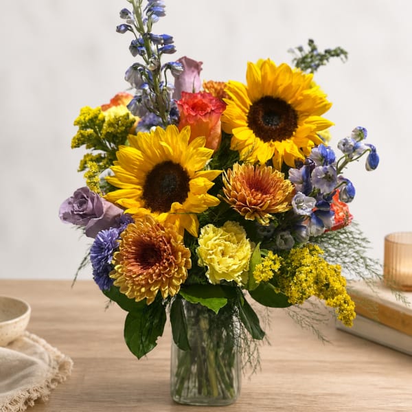 Mixed bouquet with sunflowers, chrysanthemums, and blue flowers in a glass vase