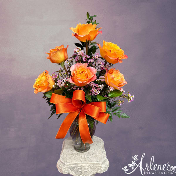 Orange roses in a glass vase with a large orange ribbon