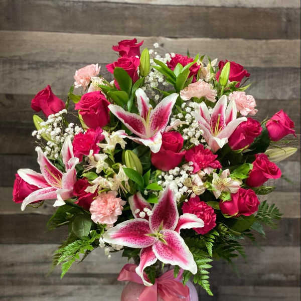 Pink roses and lilies arranged in a glass vase with a ribbon.