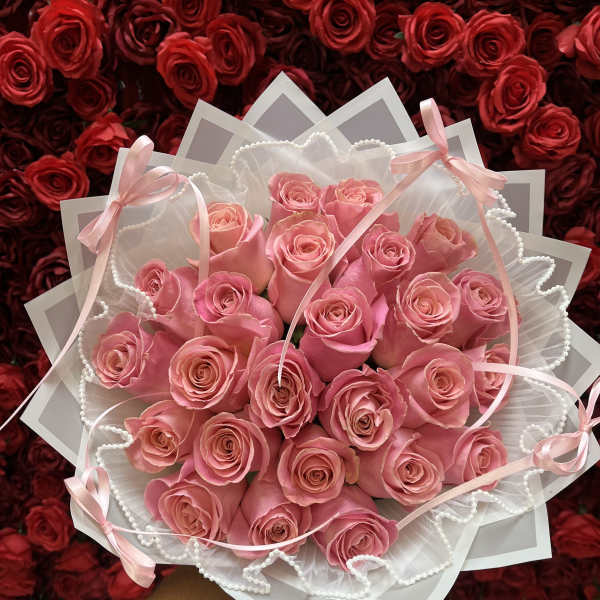 Handheld bouquet of pink roses wrapped in white paper with ribbons and pearl trim