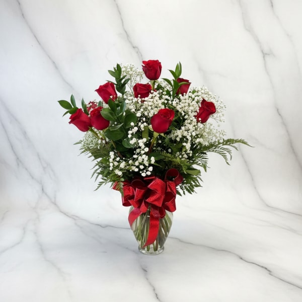 Red roses in a glass vase with baby's breath and a red ribbon