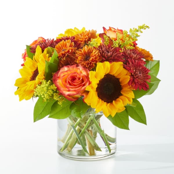 Bouquet of sunflowers, roses, and mums in a clear glass vase