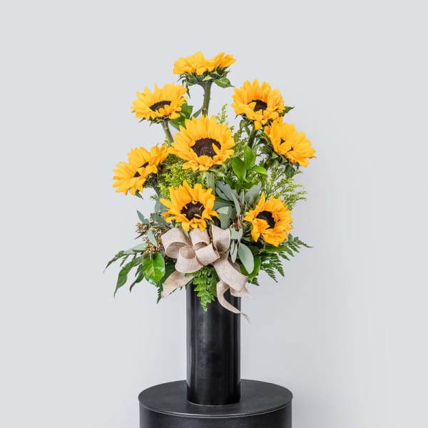 Sunflower arrangement in a tall black vase with a burlap bow