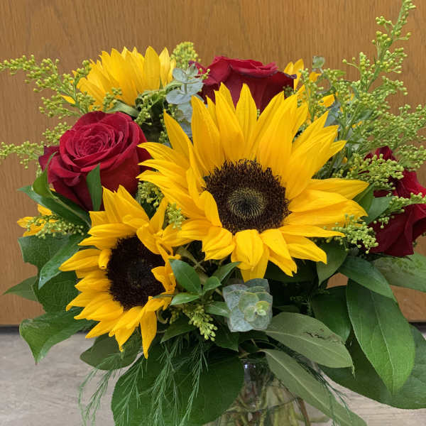 Bouquet of sunflowers and red roses in a glass vase