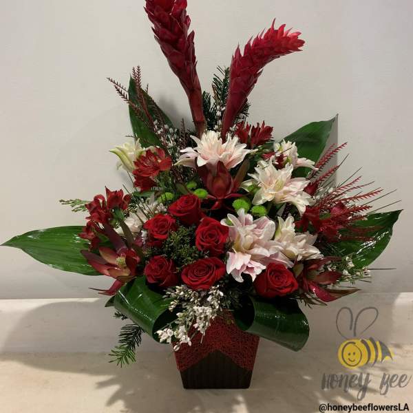 Tropical floral arrangement with red roses and white blooms in a dark vase