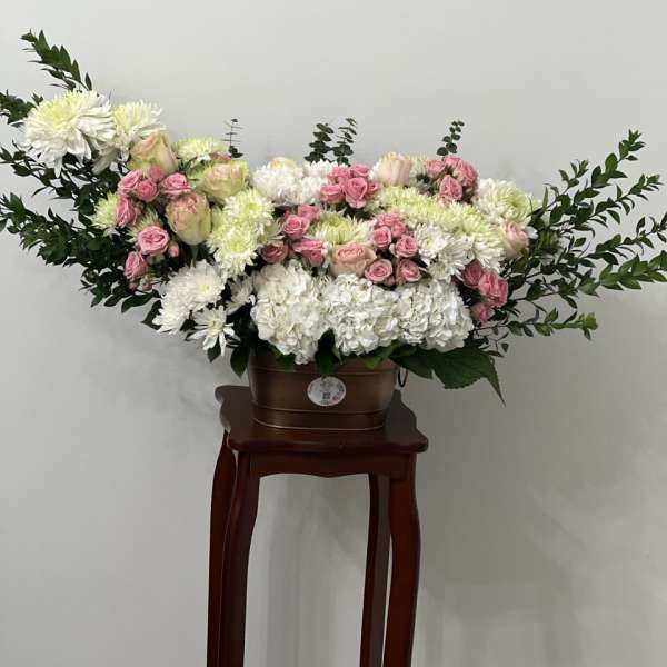 Large white and pink floral arrangement in a brown container on a stand