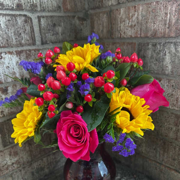 Bouquet of yellow sunflowers, pink roses, and red berries in a glass vase