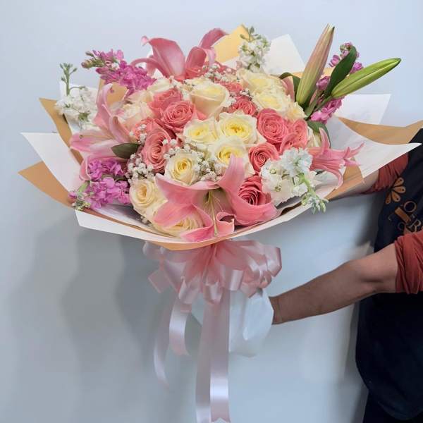 Pink and cream bouquet of roses and lilies wrapped with a ribbon