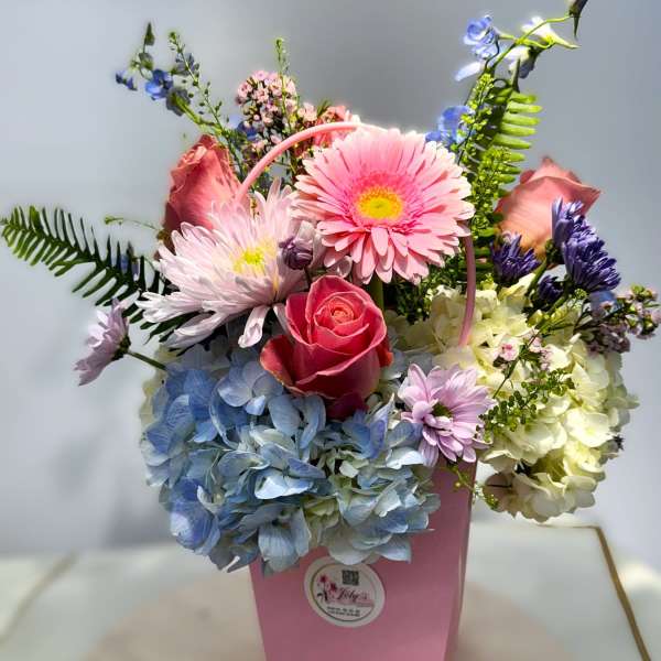 Pink and blue mixed flower arrangement in a pink box with a handle