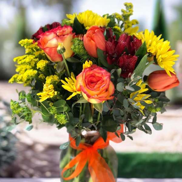 Bouquet of orange roses and yellow daisies in a glass vase with an orange ribbon