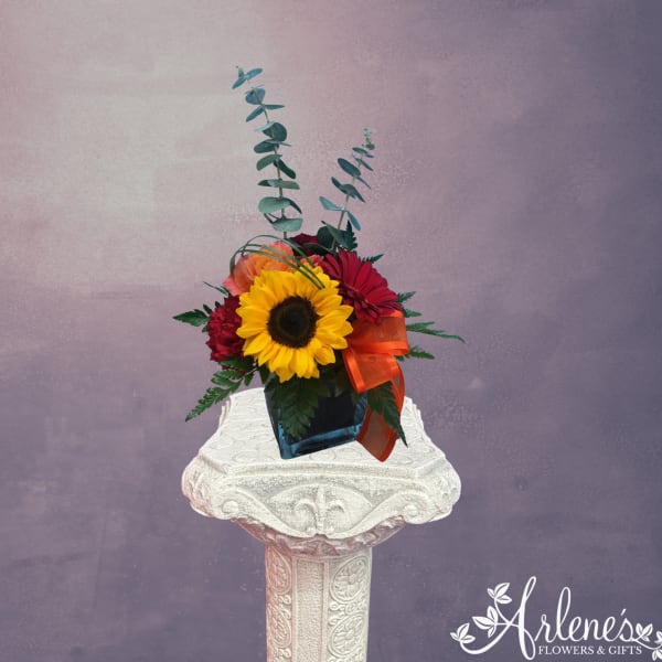 Sunflower and red flower arrangement in a blue vase with orange ribbon