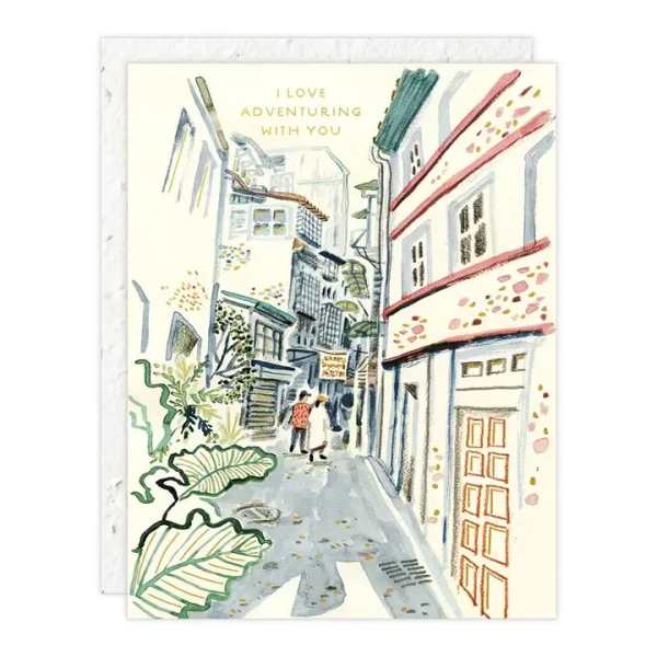 Illustrated greeting card with a narrow street scene and the text "I LOVE ADVENTURING WITH YOU"