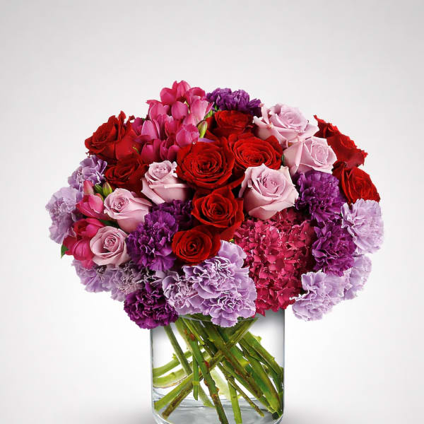 Bouquet of red and pink roses with purple carnations in a glass vase