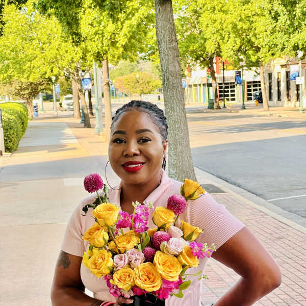 Woman holding a bouquet of yellow and pink flowers in a black vase