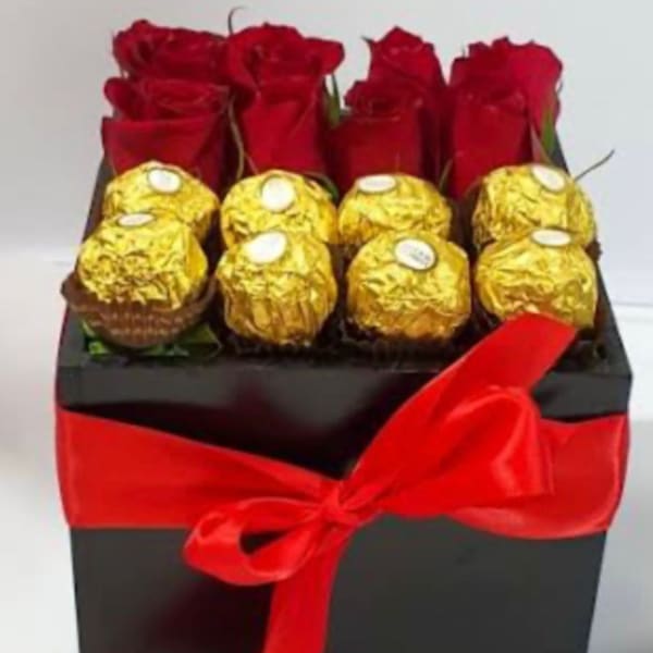 Red roses and gold-wrapped chocolates in a black gift box with a red ribbon