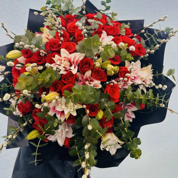 Bouquet of red roses, pink lilies, and eucalyptus with black wrap