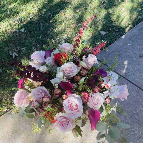 Large arrangement of light pink roses with dark pink calla lilies and mixed blooms outdoors