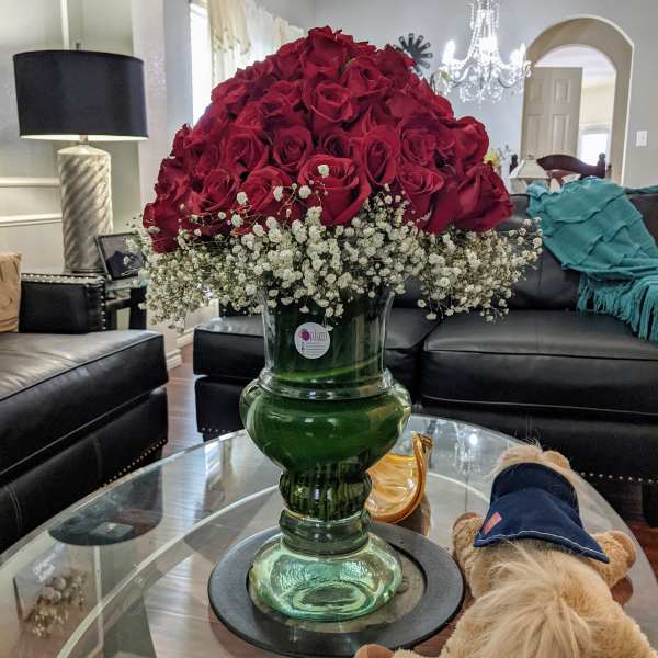 Large red rose arrangement in a green glass vase with white baby's breath