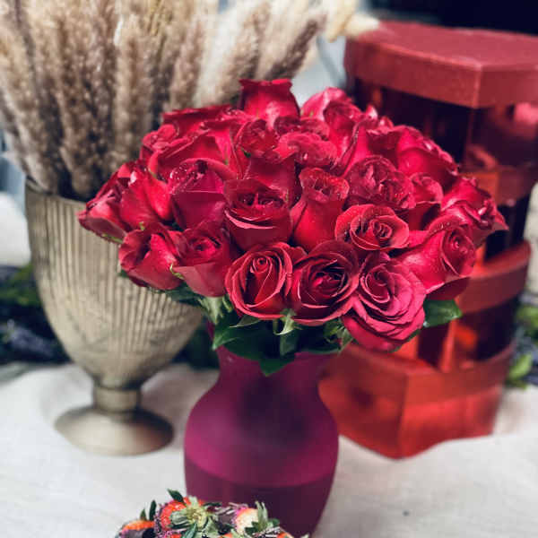 Red rose bouquet in a purple vase with chocolate-covered strawberries in front